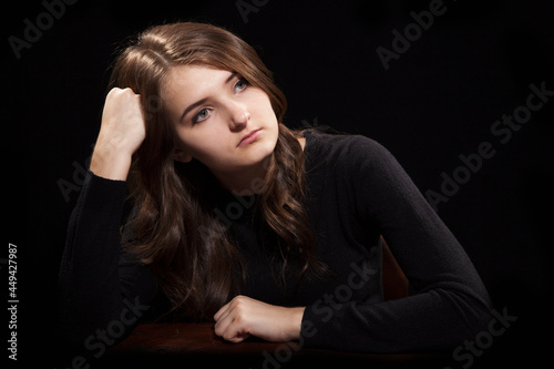 Portrait of a young girl sitting at the old table on a black background