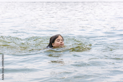A teenage girl enjoys swimming in the calm warm lake water in beautiful summer weather © Ilya