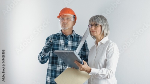 A working man in a helmet and a female engineer with a tablet and a level in their hands discuss plans for the reconstruction of the facility. Making a decision on the performance of repair work.