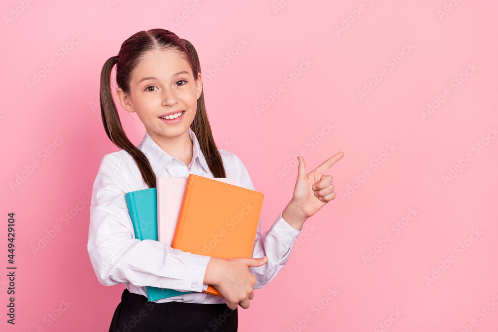 Photo of cute happy positive little girl point finger empty space hold notebook isolated on pink color background Photo of cute happy positive little girl point finger empty space hold notebook isolated on pink color background