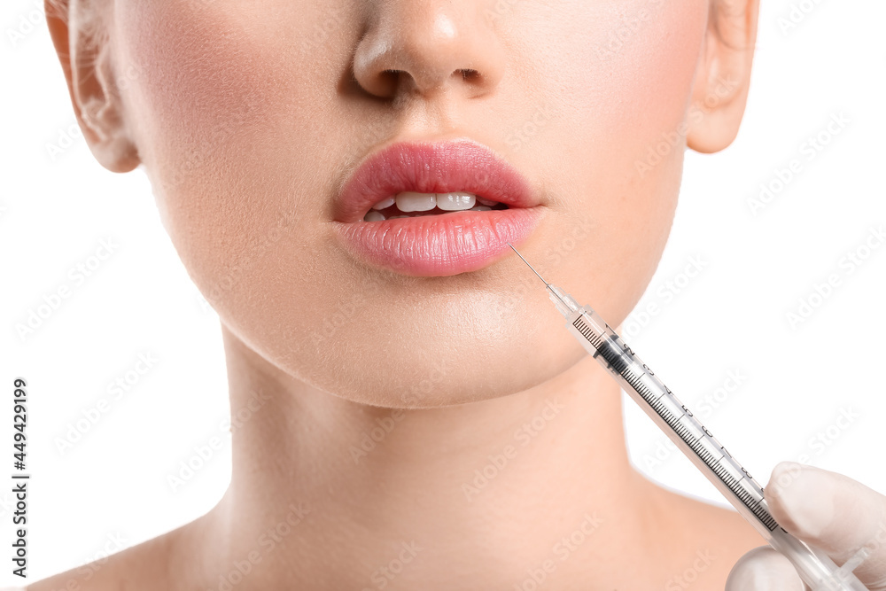 Obraz premium Young woman receiving filler injection in lips against white background, closeup