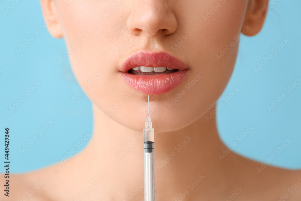 Young woman receiving filler injection in lips against color background, closeup