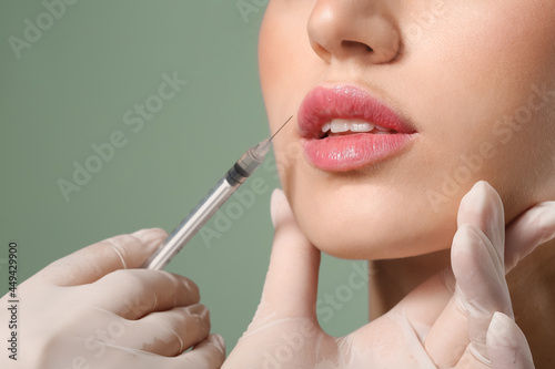Young woman receiving filler injection in lips against color background, closeup