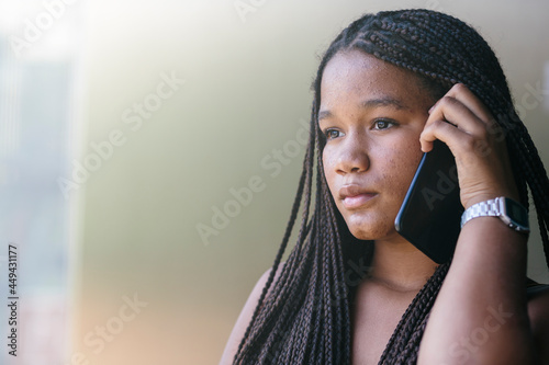 Black teenage girl with afro braided hair, talking on her cell phone, with serious, sad and dramatic expression. Adolescents, students, integration, equality and future concept. Copyspace