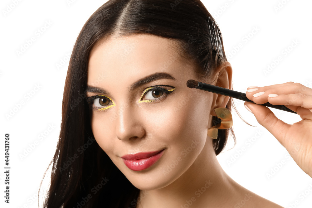 Beautiful young woman applying makeup on white background