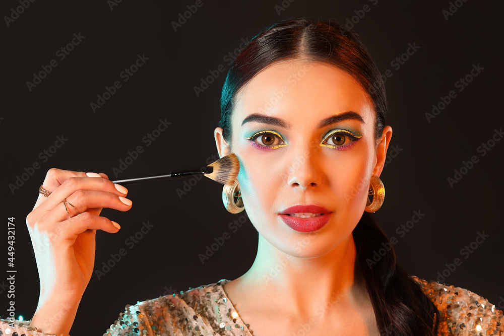 Obraz premium Beautiful young woman with makeup brush on dark background