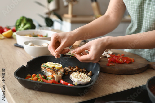 Woman cooking tasty fish and vegetables in kitchen