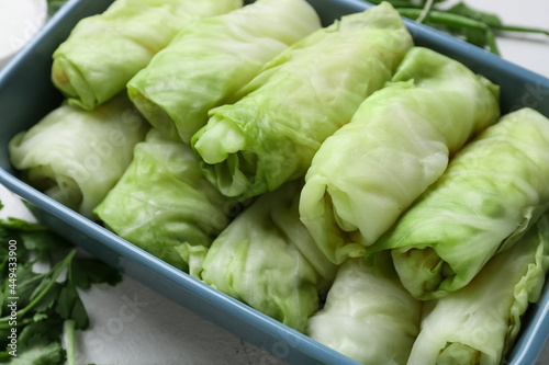 Baking dish with uncooked cabbage rolls and parsley on light background, closeup