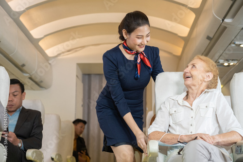Flight attendant Asian woman or air hostess take care of elderly Caucasian female passengers on the plane.
