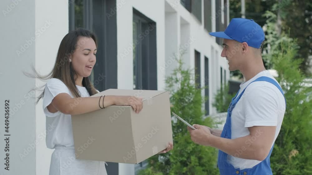 Beautiful woman meets a delivery man who gives her a parcel box beside her home, courier checks information on tablet. Home delivery, online shopping Beautiful woman meets a delivery man who gives her a parcel box beside her home, courier checks information on tablet. Home delivery, online shopping
