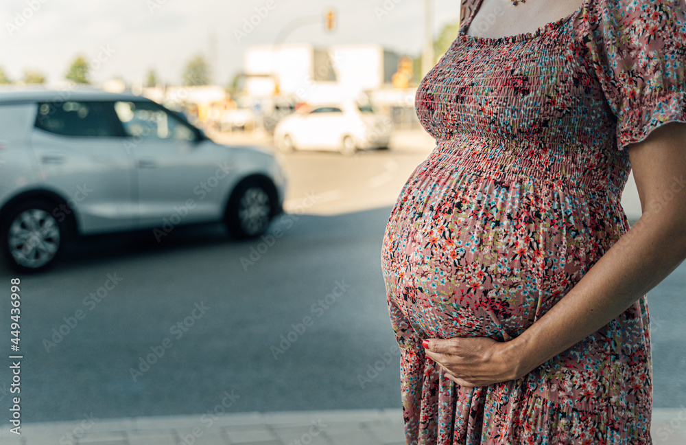 Close-up of a pregnant belly with a city street on the background