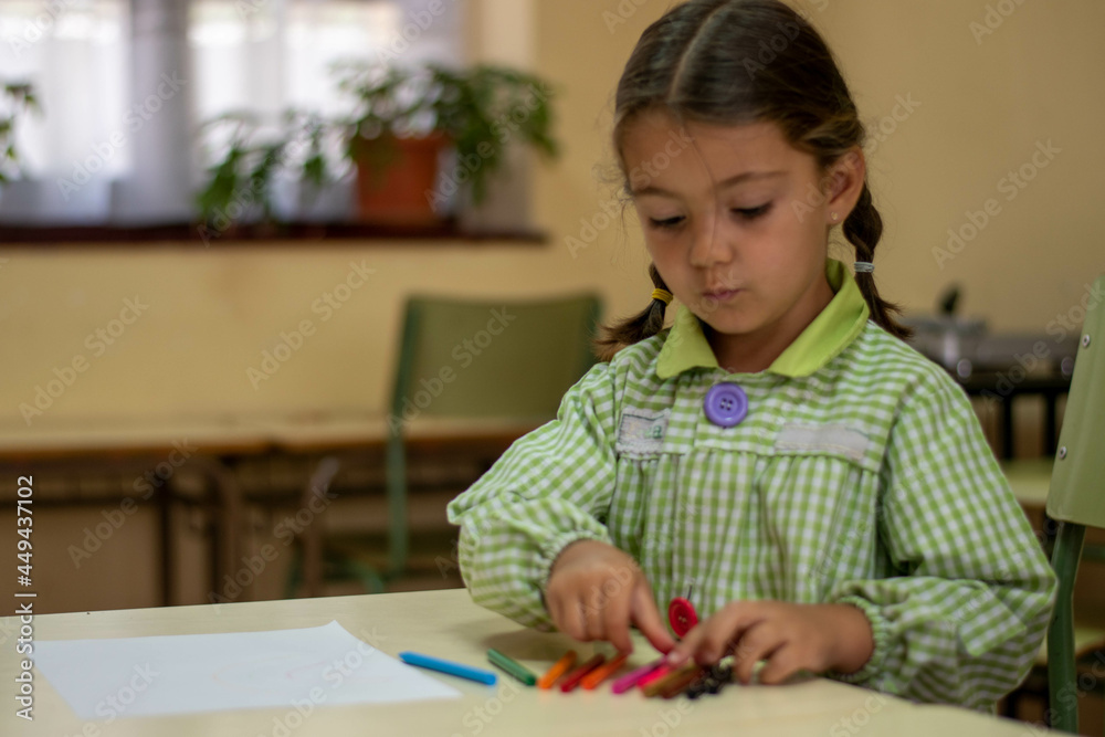 Adorable niña en su primer día de colegio vestida con mandilón a cuadros verdes dibujando y mirando libros. Adorable niña en su primer día de colegio vestida con mandilón a cuadros verdes dibujando y mirando libros.