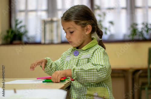Adorable niña en su primer día de colegio  vestida con mandilón a cuadros verdes dibujando y mirando libros.