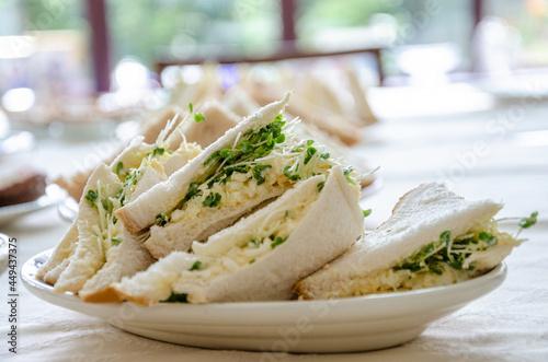 A plate of triangular cut egg and cress sandwiches on a plate on a table as part of a buffet lunch