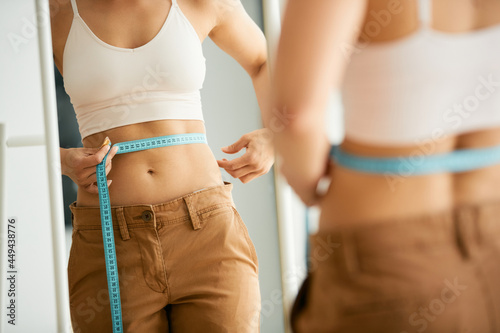 Reflection in a mirror of slim woman measures her waist with tape measure. photo