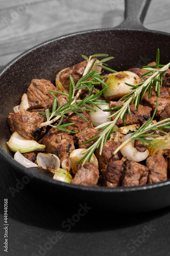 Diced Aberdeen Angus beef with shallots and rosemary, fried in a cast iron frying pan. Selective colour image
