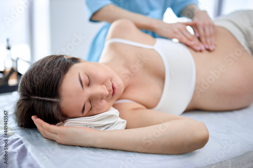 Close-up view on pregnant woman receiving massage on belly my female masseur, enjoying with eyes closed, having rest during spa treatment