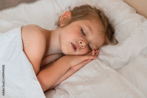Adorable little girl sleeping in bed with white linens. Place for your text. Healthy baby sleep.