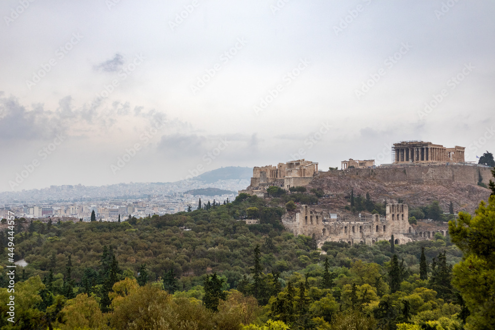 Acropolis hill (Parthenon, Propylaea, Temples, Odeon of Herodes Atticus) and white city in summer greenery. Athens ancient historical landmark from Filopappou Hill on cloudy day