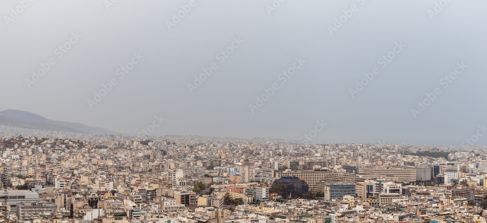 Panorama of Athens city center overcrowded streets with white buildings architecture on cloudy foggy day. Rooftop view from Filopappou Hill near Acropolis, Greece