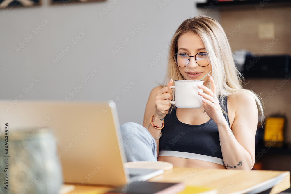 CAucasian freelancer woman work from home. Female hold tea chatting or watching movie use laptop. Modern girl relaxing at kitchen surfing internet CAucasian freelancer woman work from home. Female hold tea chatting or watching movie use laptop. Modern girl relaxing at kitchen surfing internet