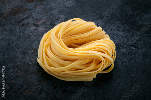 Fresh raw tagliolini pasta rolled with a nest on a stone background. Type of Italian pasta