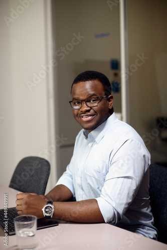 Happy black entrepreneur works on laptop in office and looking at camera.