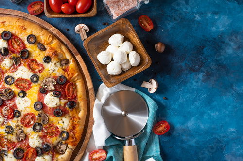 A beautiful still life of pizza, ingredients and a pizza knife. Dark blue background. View from above. Low angle view. Pizzeria, restaurant, cafe. Fast food.Advertising business.