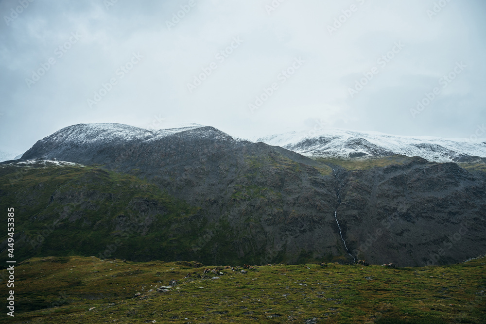 Minimalist alpine landscape with snowy mountains in low cloud in overcast weather. Deep gorge on background of snowbound mountain range under low cloudy sky. Atmospheric minimalism in high mountains.