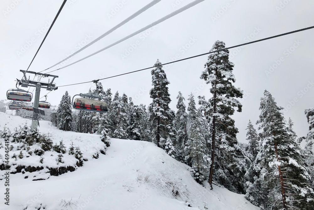 Outdoor four-seater lift rises above the ski slope in high white winter mountains, ski season, winter activities Outdoor four-seater lift rises above the ski slope in high white winter mountains, ski season, winter activities
