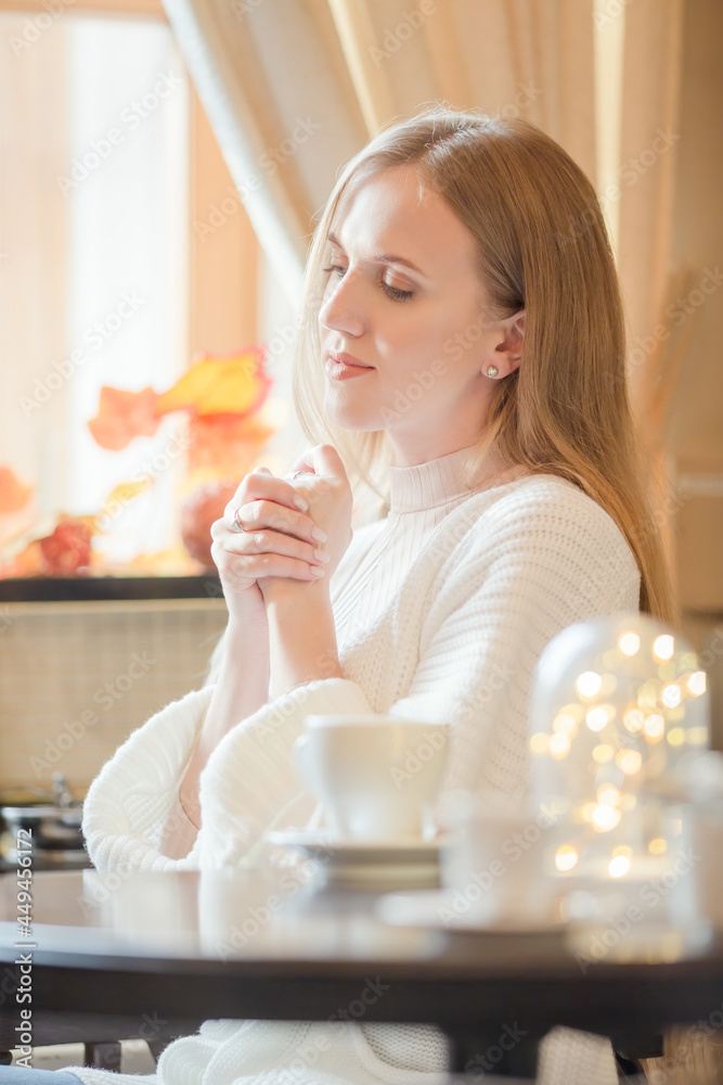 Portrait of an attractive woman in a white knitted jacket. A beautiful dreamy young woman is waiting in a cozy cafe or at home. Closeup. Shallow depth of field. Soft focus and blurry background. Portrait of an attractive woman in a white knitted jacket. A beautiful dreamy young woman is waiting in a cozy cafe or at home. Closeup. Shallow depth of field. Soft focus and blurry background.