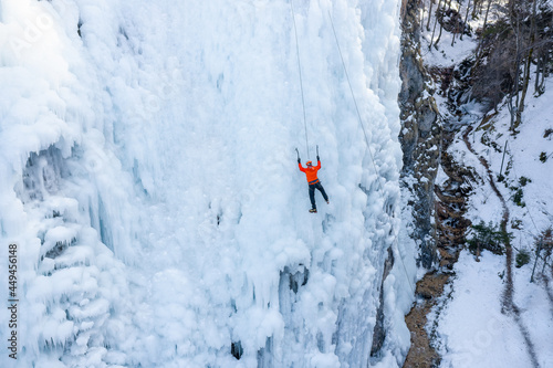 Aerial shot of an ice slope bumps, ridges, and icicles by which climbing up Caucasian man using traction ice tool technique