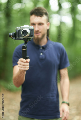 Young artist with dreadlocks holding up his digital camera on a gimbal, a handheld stabilizer, getting ready to shoot some footage in a forest