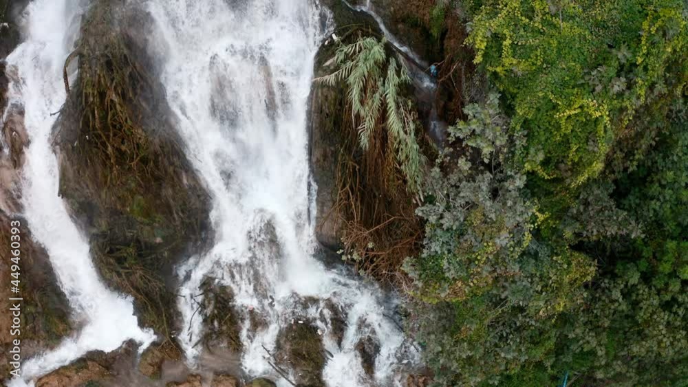 Beautiful mountain Turkish waterfall view from above. Waterfall in the rock with a lot of plants shooting from a drone. The flow of water from the mountain breaks on the ground and stones Beautiful mountain Turkish waterfall view from above. Waterfall in the rock with a lot of plants shooting from a drone. The flow of water from the mountain breaks on the ground and stones