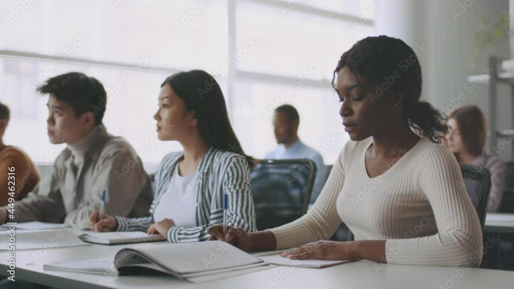 Group of young multiethnic university students taking notes, sitting together and classroom during lecture, slow motion Group of young multiethnic university students taking notes, sitting together and classroom during lecture, slow motion