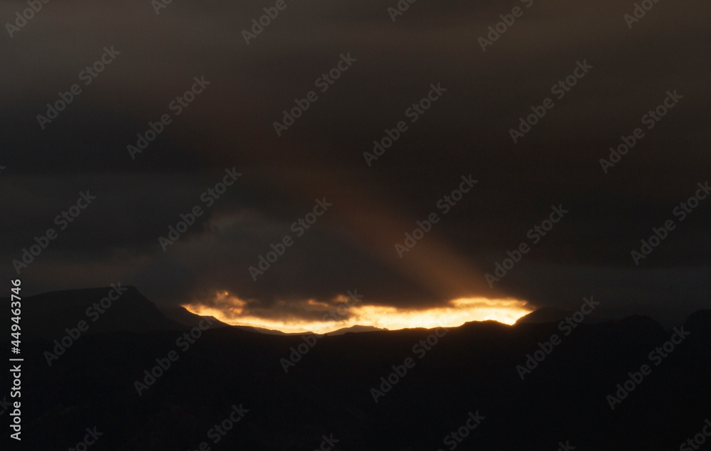 Dark cloudscape. View of the dramatic sunset with dark clouds. The last bright ray of sunlight strikes across the sky and mountains silhouette.  