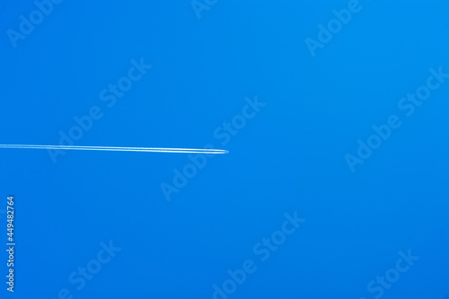 A plane is flying in a clear blue sky leaving a trail behind it