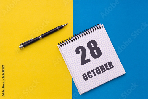 October 28th. Day 28 of month, calendar date. Notebook with a spiral and pen lies on a yellow-blue background