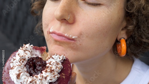 Close up of a young female taking a bite of vegan berry doughnut and chews it with face covered in frosting with her eyes closed 