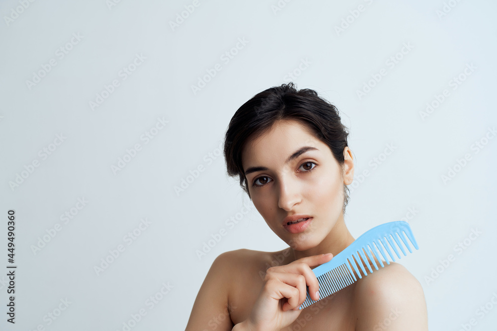 Obraz premium brunette with bare shoulders combs hair grooming light background
