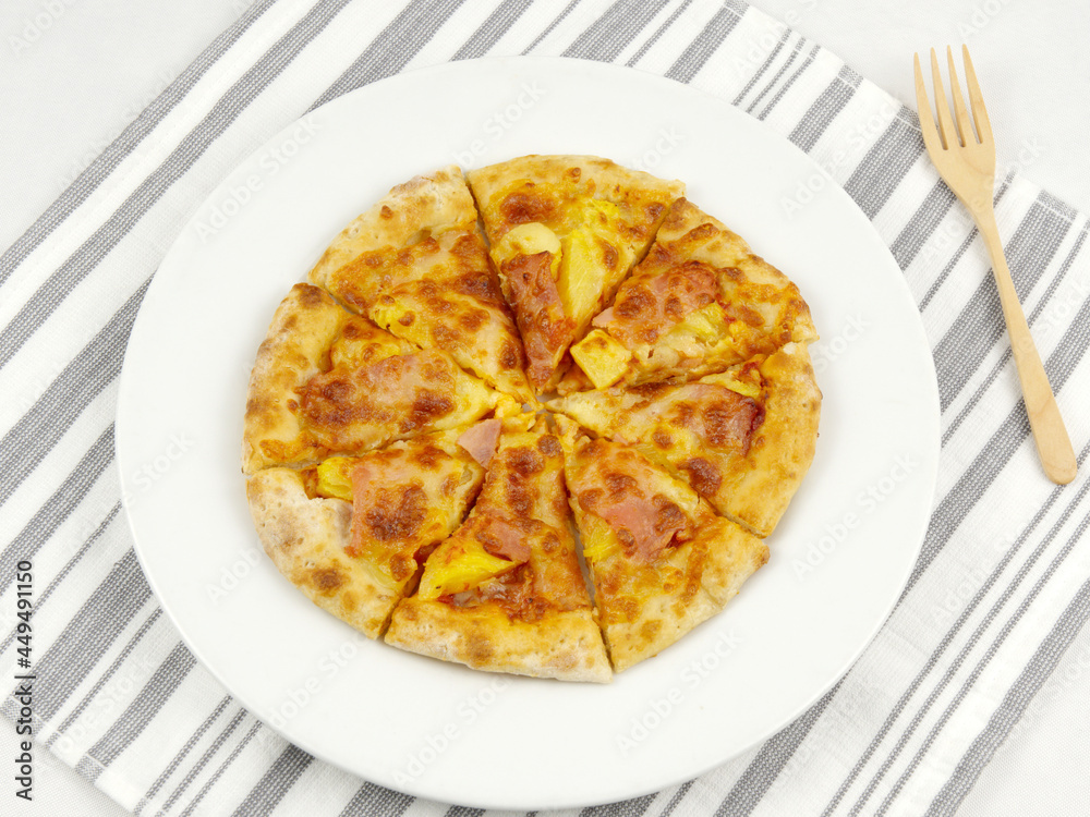 Top view of homemade pizza on a white plate and a fork on a gray and white striped napkin