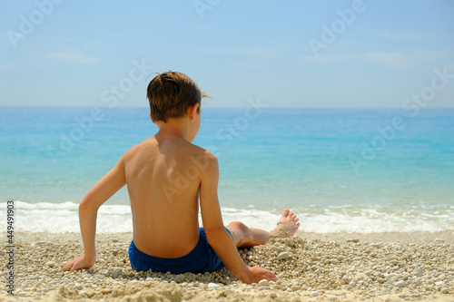 Young boy sitting on a beautiful beach during summer vacation in Greece