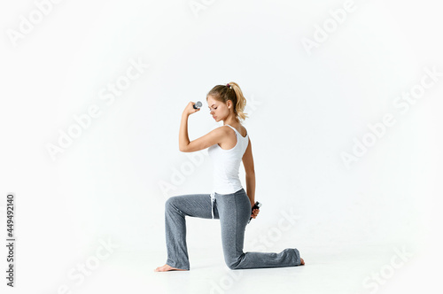 athletic woman sitting on the floor barefoot dumbbell workout light background
