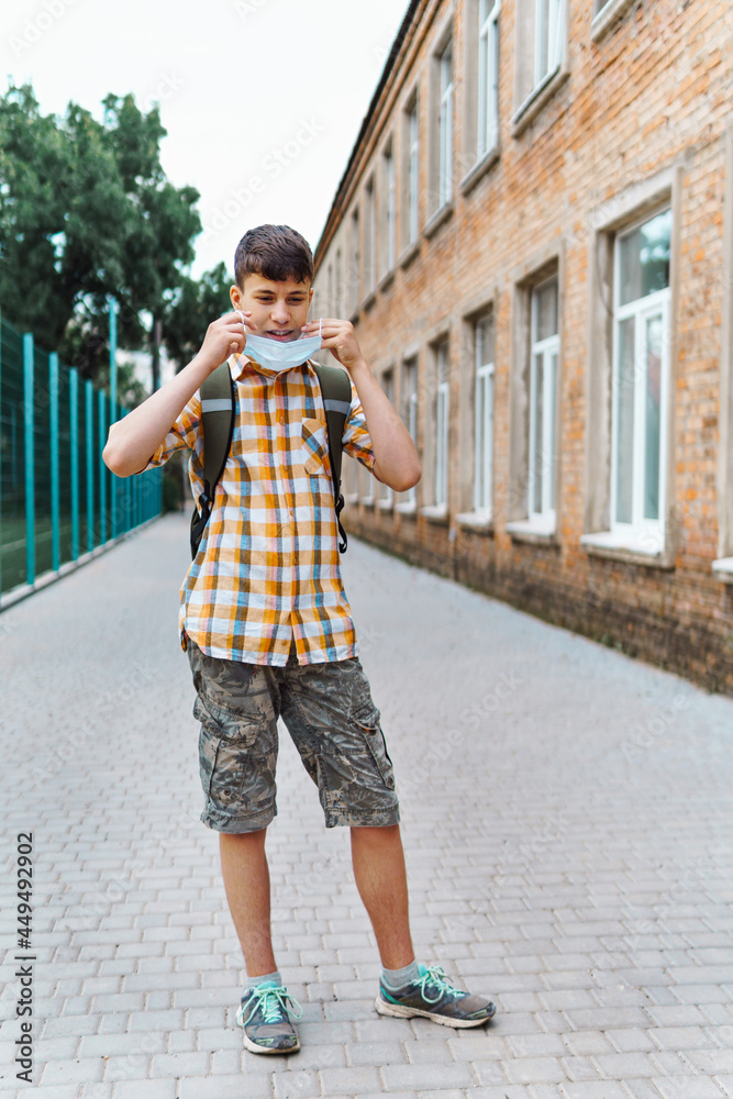 schoolboy poses in the backyard of the school, wearing a protective mask on his face from a coronavirus infection, education and back to school concept schoolboy poses in the backyard of the school, wearing a protective mask on his face from a coronavirus infection, education and back to school concept