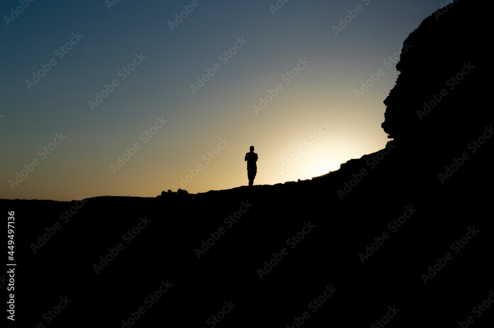 Silhouette of man on a rock with the sun back light, silhouette of a person on a rock, entrepreneurship concept