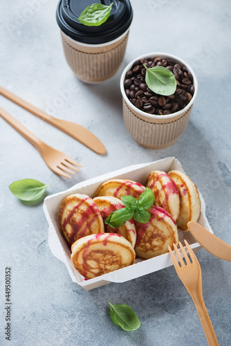 Pancakes in a takeaway carton container with coffee, elevated view on a light-blue stone background, vertical shot