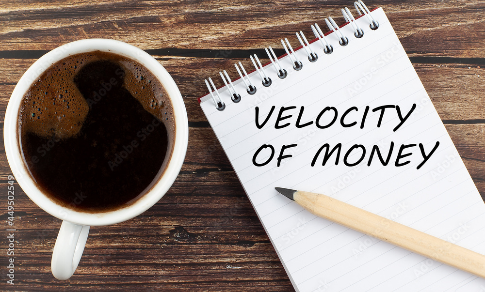 VELOCITY OF MONEY text on notebook with coffee on wooden background VELOCITY OF MONEY text on notebook with coffee on wooden background