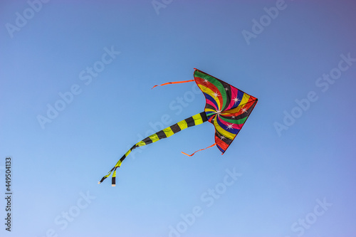 A brightly multi-colored kite flies in the wind high in the sky. Children's entertainment, outdoor fun for kids in the summer. A concept of freedom, joy, summer vacation, holidays at a children's camp