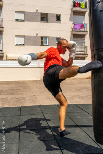 Muscular man punching with leg a boxing bag on cross fit training at the street. Training concept © Andres