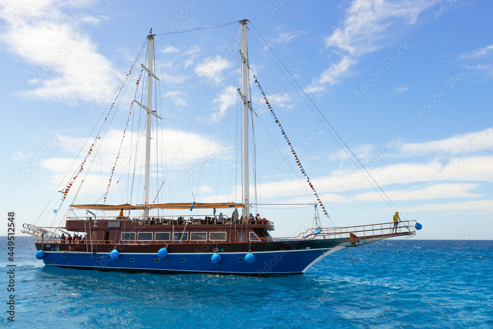 A pleasure sailboat plows the azure waters of the Red Sea, an imitation of a pirate ship, the sails are lowered, the blue sky with white clouds A pleasure sailboat plows the azure waters of the Red Sea, an imitation of a pirate ship, the sails are lowered, the blue sky with white clouds